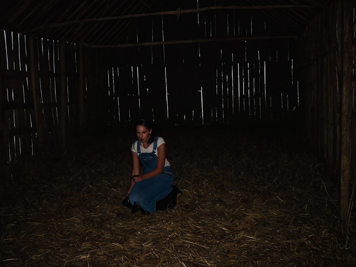 Young Woman in Dim Barn with Somber Atmosphere