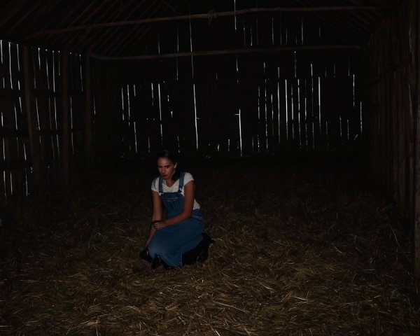 Young Woman in Dim Barn with Somber Atmosphere