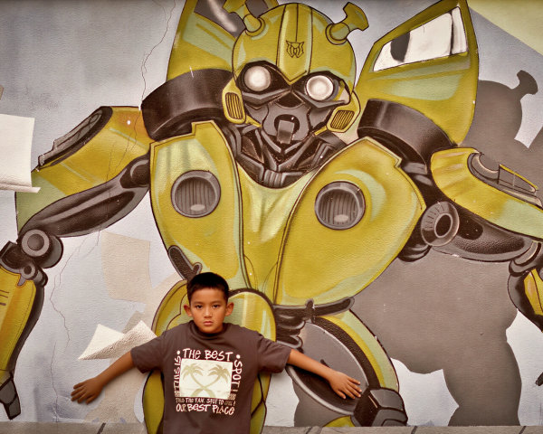 Boy in front of glowing robot graffiti on concrete wall