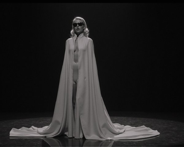 Elegant Figure in Spotlight with White Cape on Stage
