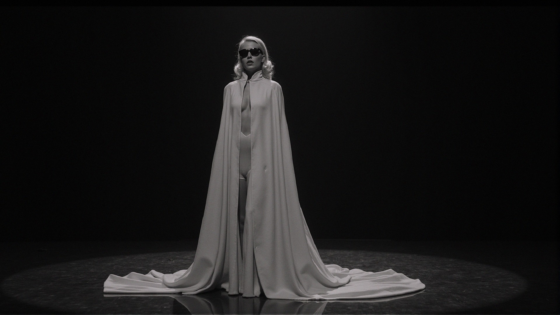 Elegant Figure in Spotlight with White Cape on Stage