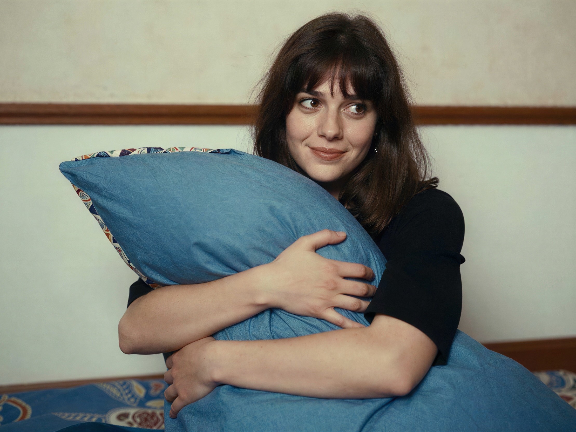 Young woman with dark hair holding a blue pillow
