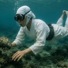 Diver in White Outfit Explores Underwater Coral Scene