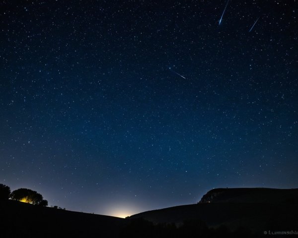 Night Sky with Stars and Meteors Over Rolling Hills