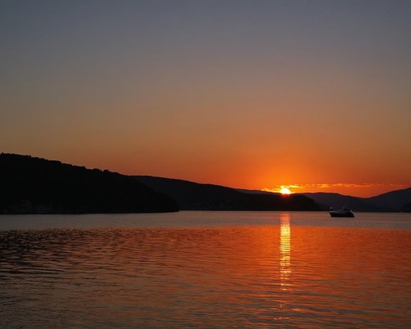 Vibrant Sunset Over Calm Waters with Silhouetted Hills