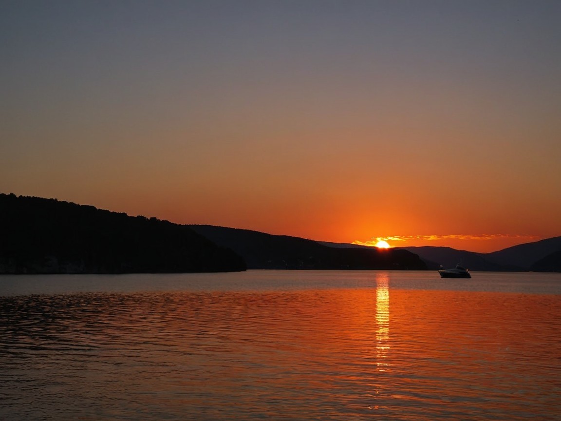 Vibrant Sunset Over Calm Waters with Silhouetted Hills