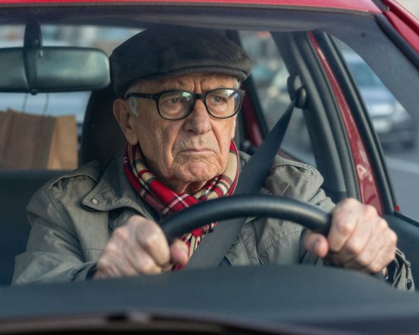 Elderly man driving a red car with focused expression