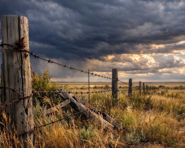 Dramatic Photograph of Fence in Grassy Field with Clouds