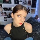 Woman with Cat Ear Headband and Striking Makeup Beside Black Cat in Electronic-Filled Room