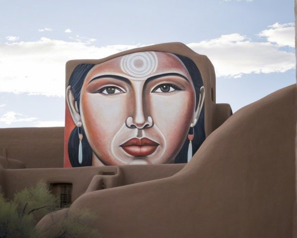 Mural of a woman's face on a building with desert plants