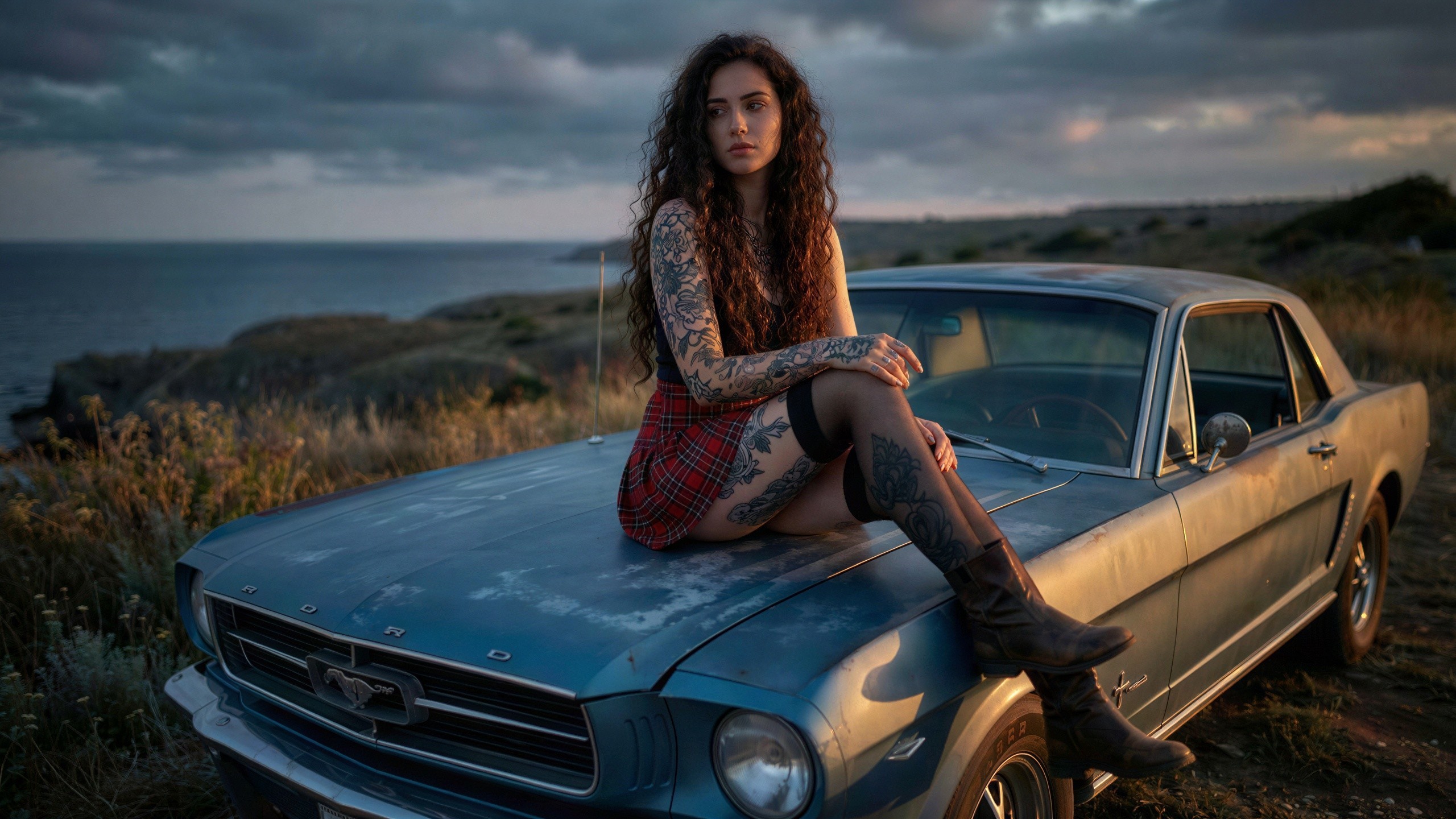 Woman with tattoos sitting on vintage Mustang at ocean cliff