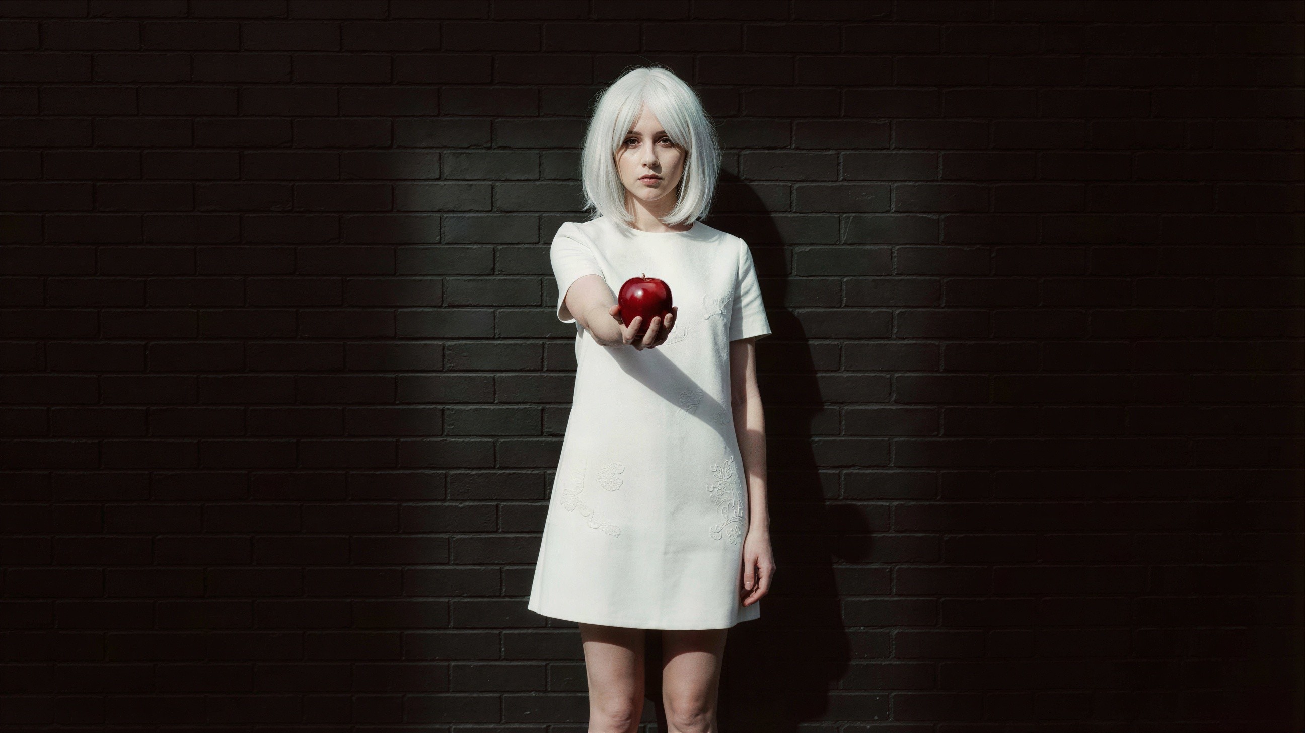 Young woman in white dress holding red apple against wall