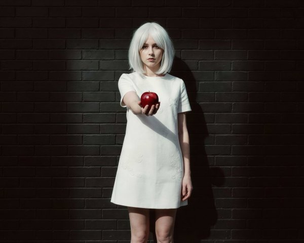 Young woman in white dress holding red apple against wall