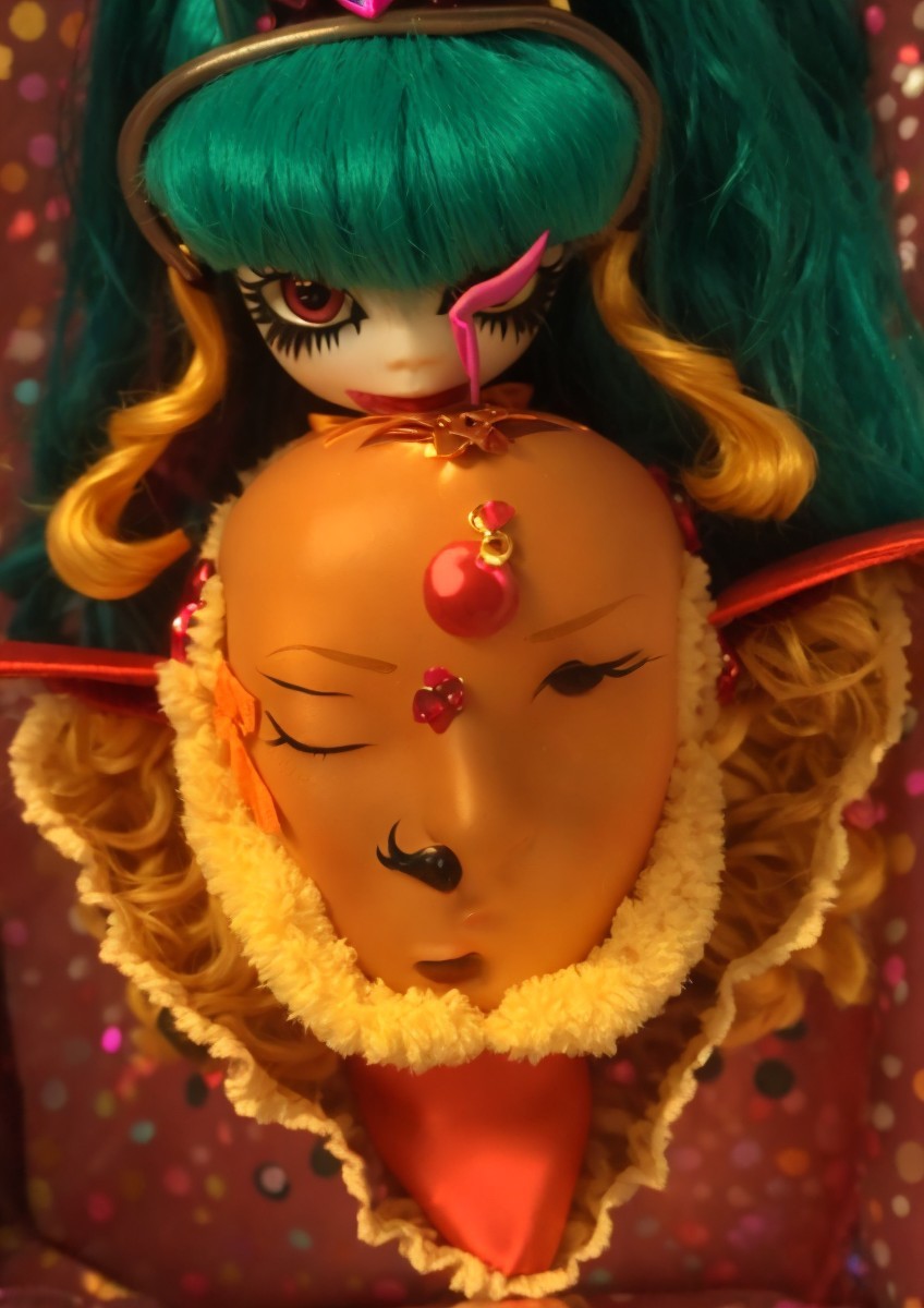 Stylized doll with teal hair and vibrant orange mask