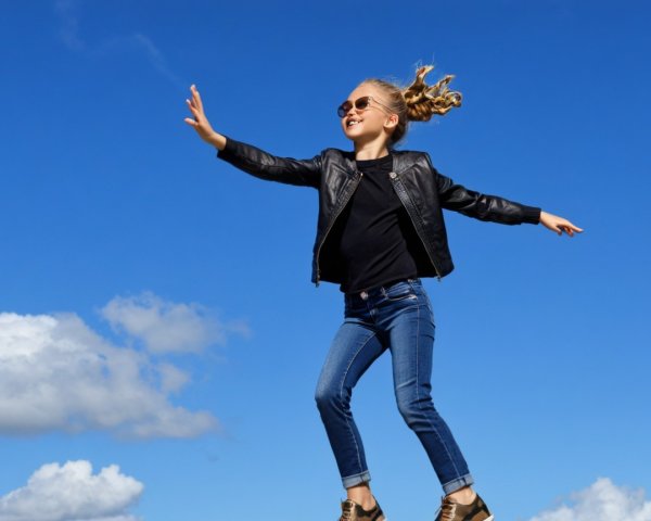 Young girl in leather jacket leaps against blue sky
