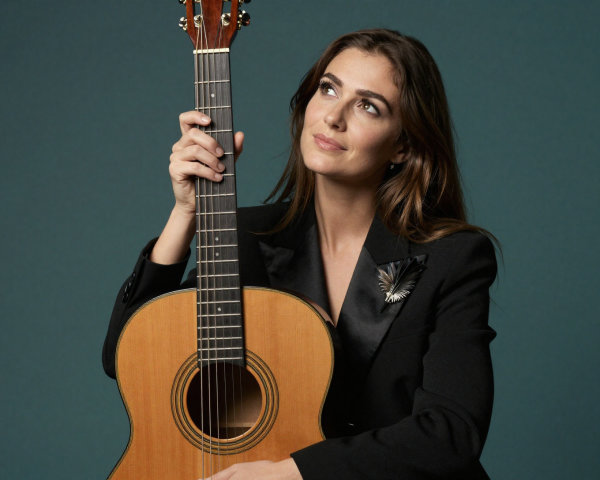 Light-skinned woman with guitar in dark teal setting