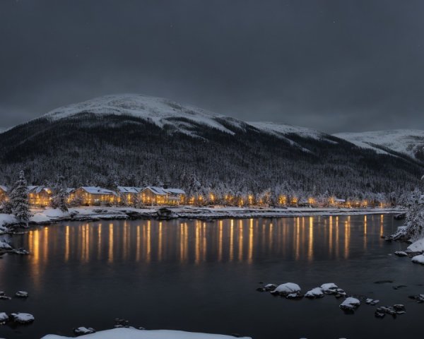 Snowy Mountain Resort Town at Night with River Reflection