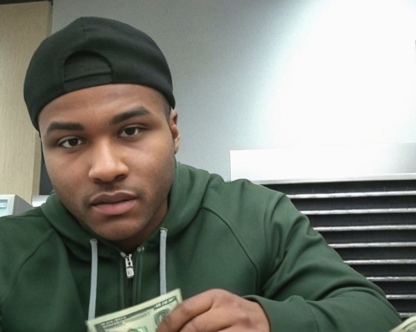 Man in Black Cap and Green Hoodie Holding Dollar Bill