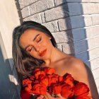 Elegant woman in red top poses against white wall