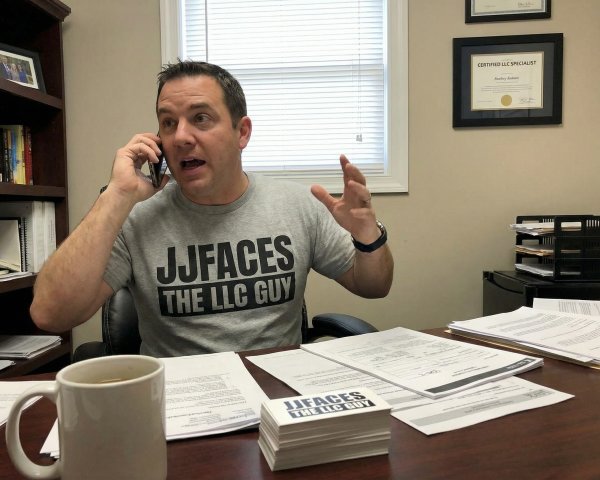 Man in Grey T-Shirt at Desk with Phone and Papers