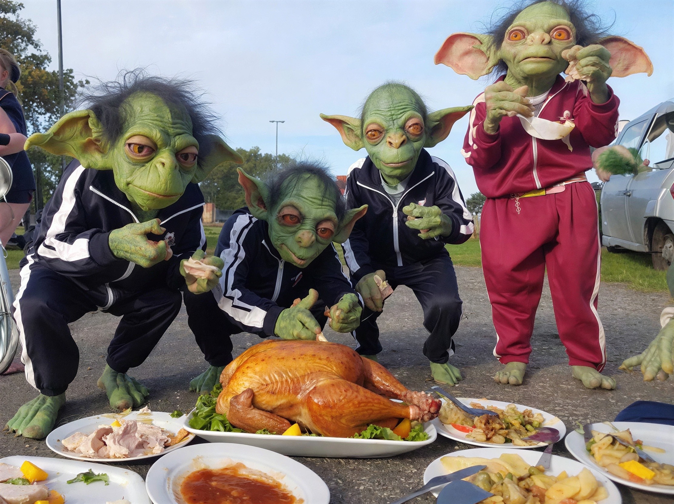 Goblin-like figures in tracksuits at a feast outdoors