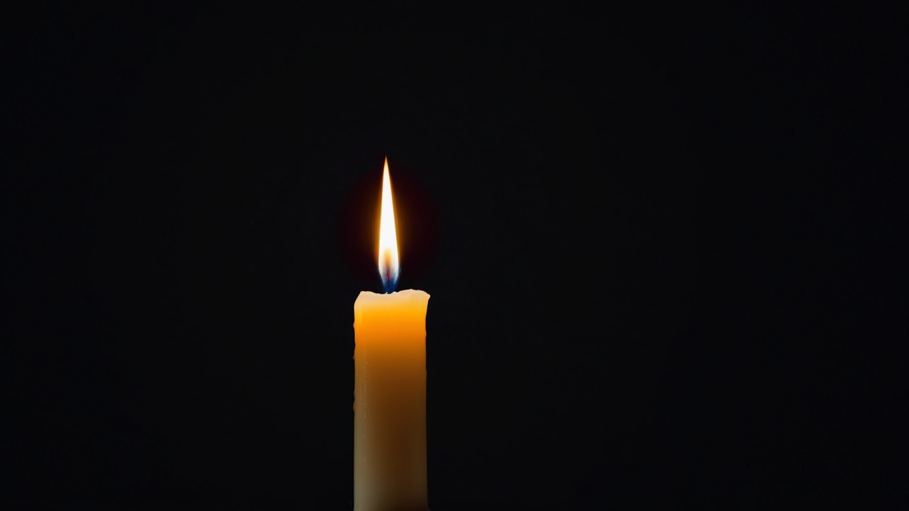 Solitary Candle Against Dark Backdrop with Flickering Flame