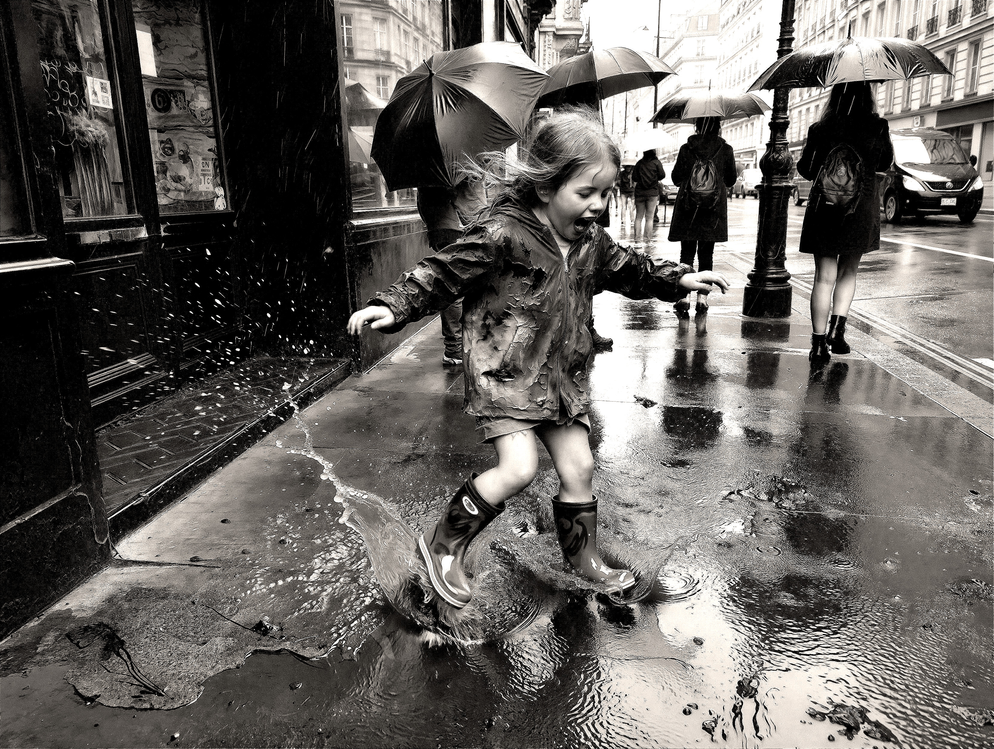Black and white street photo of a child jumping in puddle