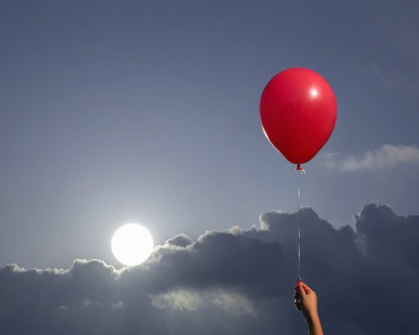 Hand Holding Red Balloon Against Dramatic Sky