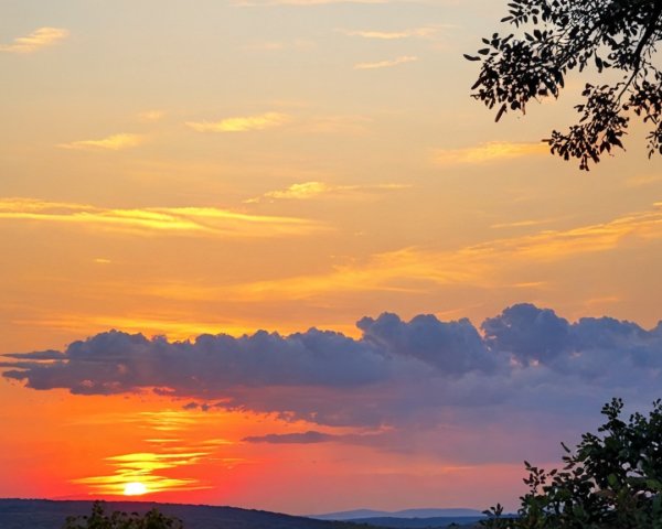 Vibrant Sunset with Silhouetted Clouds and Landscape