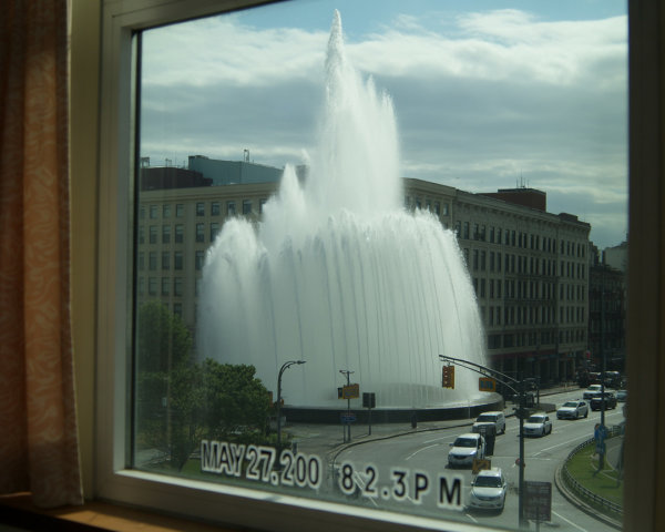 Fountain Display Against Urban Skyline and Traffic