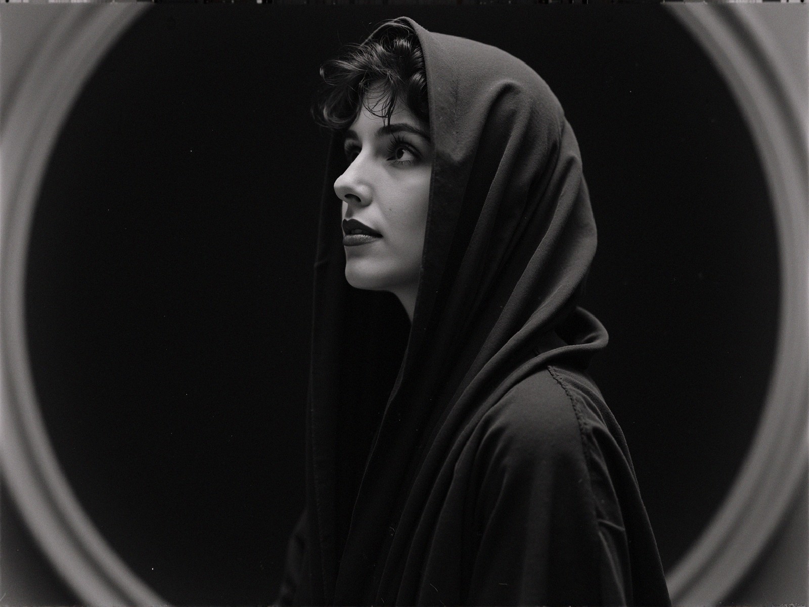 Profile of a woman in dark hooded garment with light backdrop