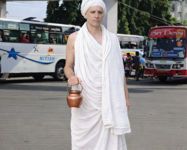 Light-skinned male in toga at bus stop with copper pot