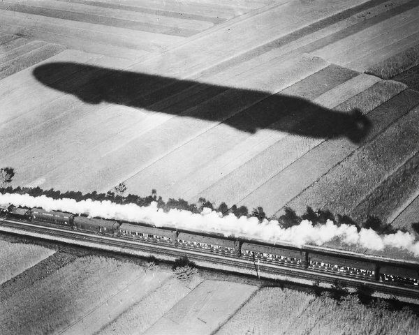 Steam train and zeppelin over patchwork landscape