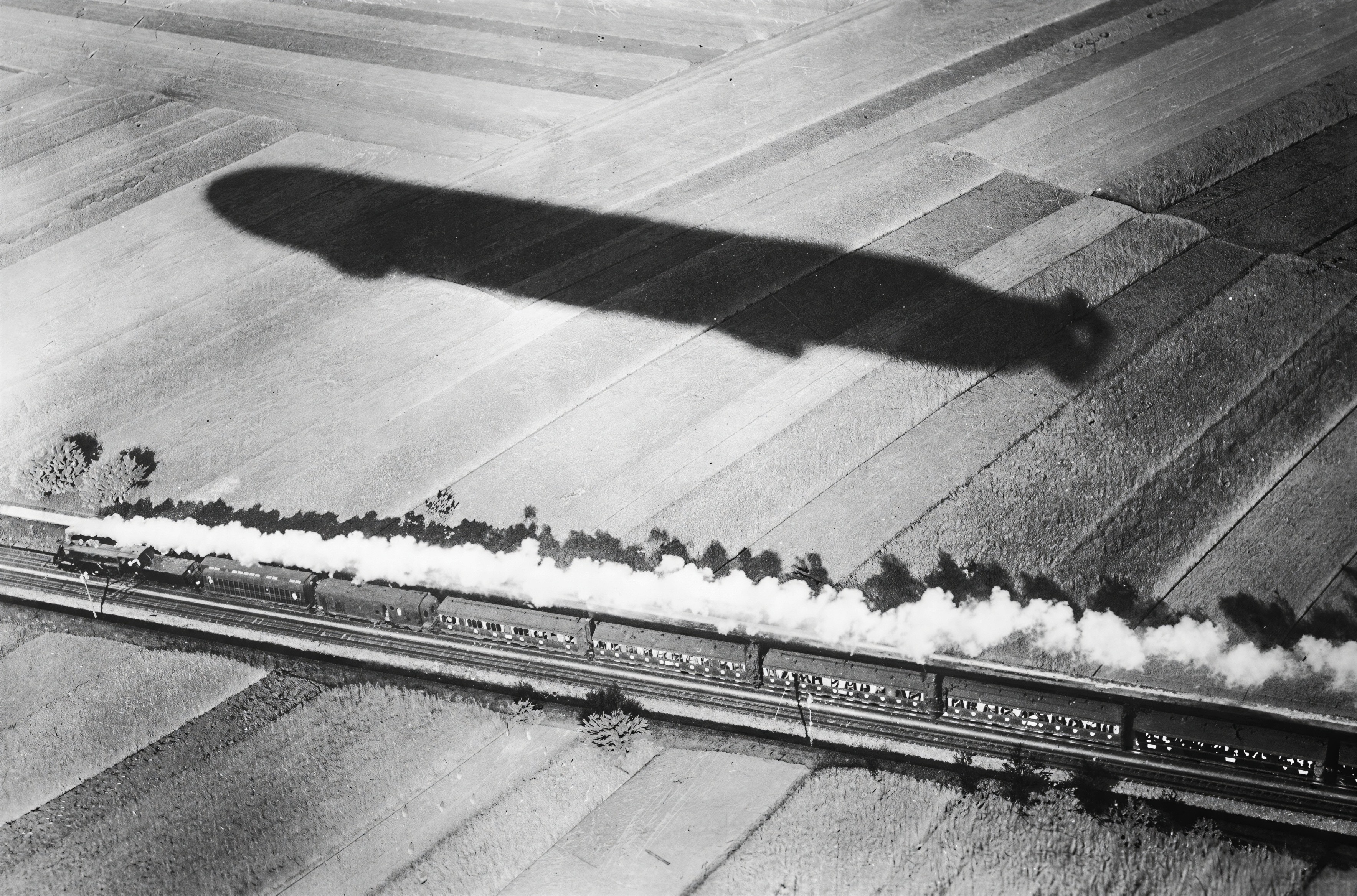 Steam train and zeppelin over patchwork landscape